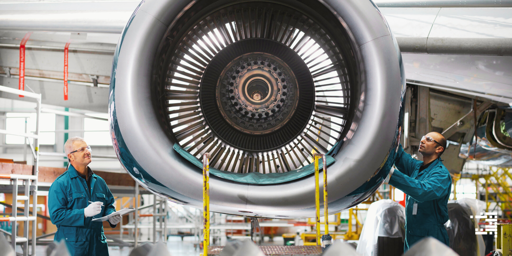 Two workers inspecting an airplane engine in a hangar.