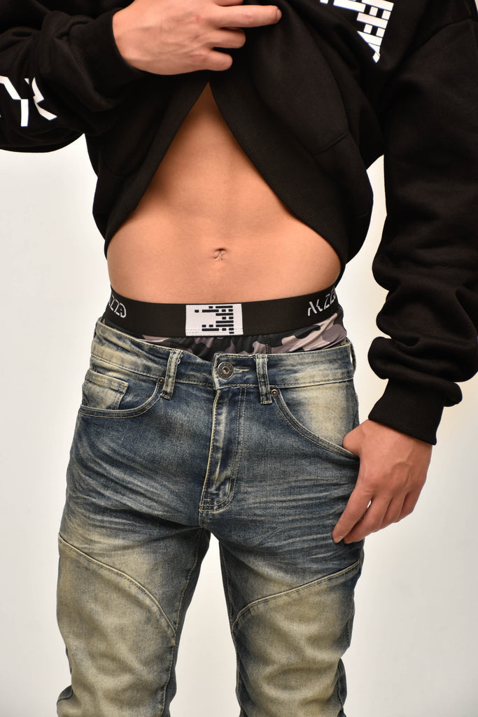 Person wearing a black hoodie and blue jeans with a visible brand logo on the waistband.